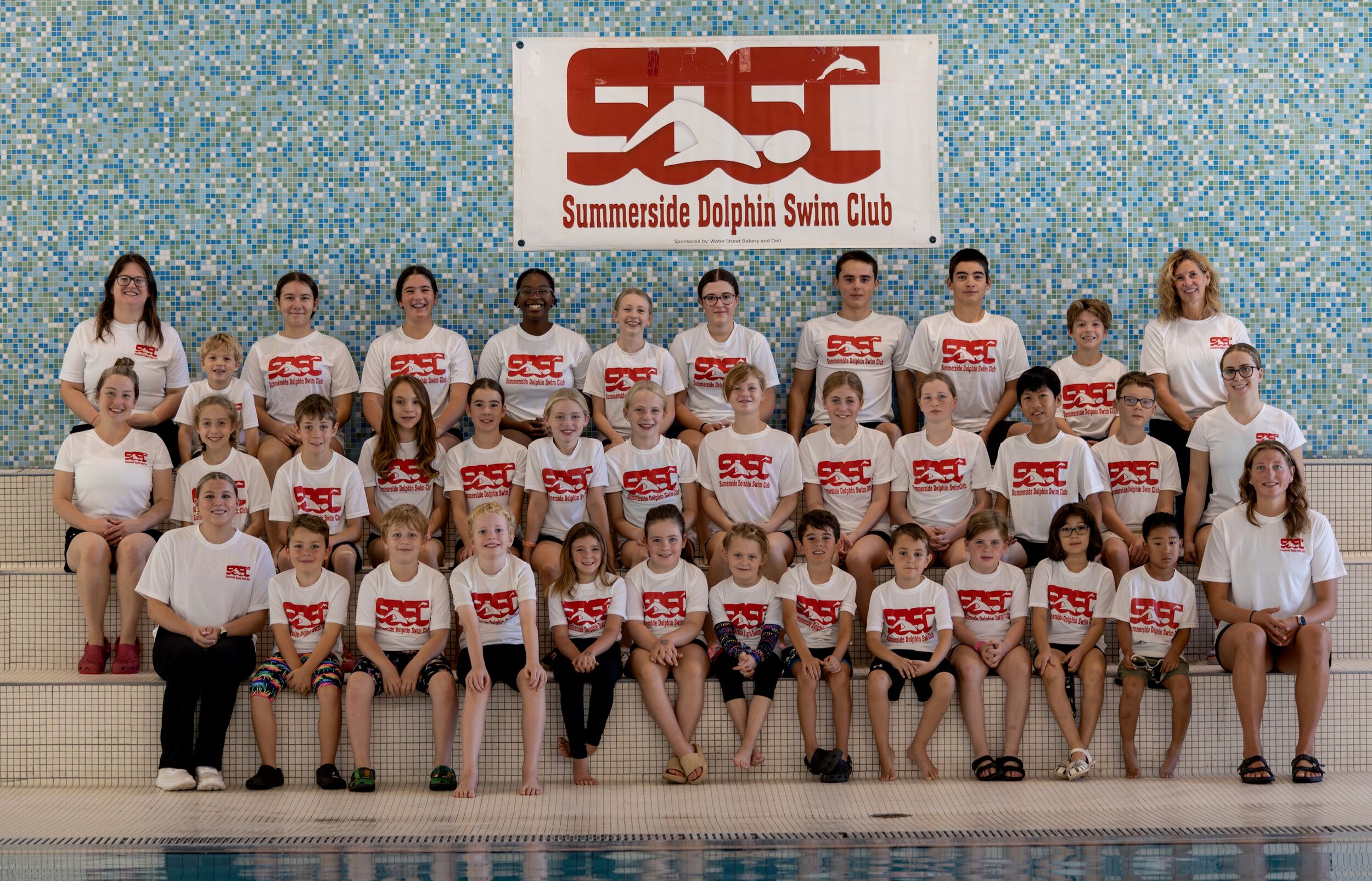 Group of young swimmers on deck wearing SDSC t-shirts and swim caps.