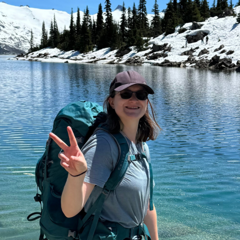 Jess Godfrey with a blue hat and sunglasses in with a lake and snow in the background